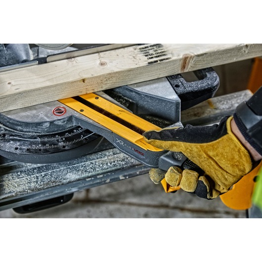 Close-up of a gloved hand operating a DEWALT XR FLEXVOLT miter saw to cut a wooden plank, with sawdust visible on the tool.