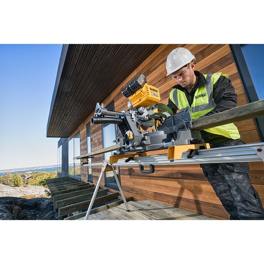 A construction worker wearing a safety helmet and high-visibility jacket operates a DEWALT DHS780T2A power saw mounted on a