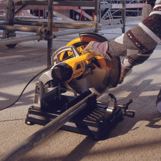 A DEWALT DT1922 power saw being used to cut a metal pipe on a construction site. The saw is mounted on a black base, and the