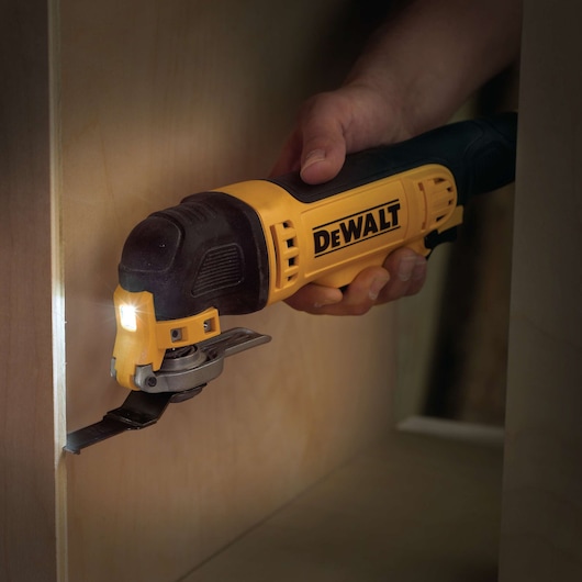 A DEWALT oscillating multi-tool being used to cut a piece of wood, held by a person’s hand.