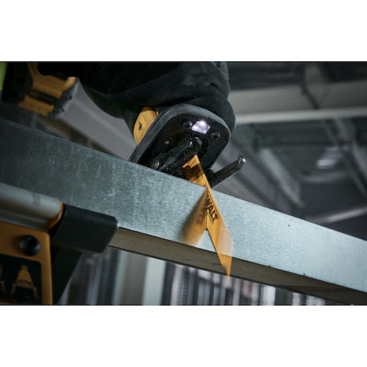 Close-up of a DEWALT reciprocating saw cutting through a metal beam, with a visible yellow saw blade labeled DEWALT.