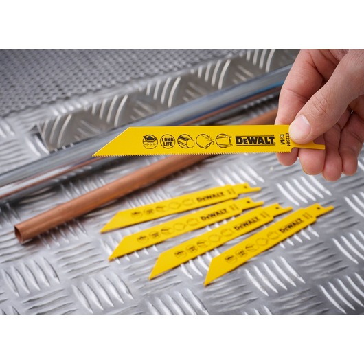 Yellow DEWALT reciprocating saw blades DT2384 displayed on a metal surface, one held by hand, pipes in background.