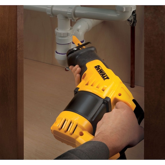 Hands using a DEWALT reciprocating saw to cut plastic pipes under a sink.