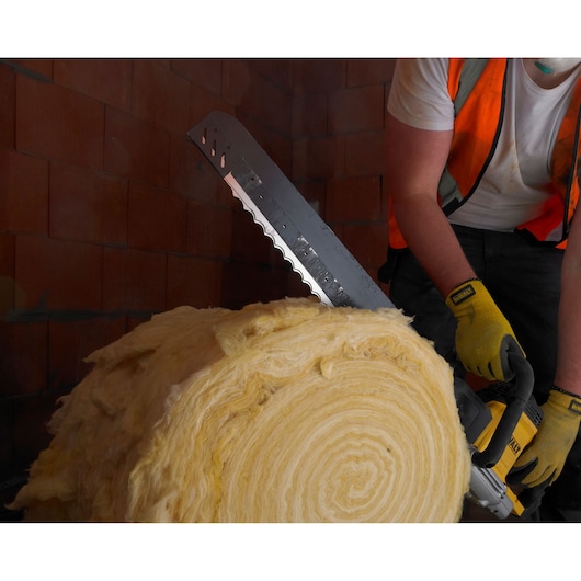 A person wearing a safety vest and gloves uses a DEWALT electric saw with a serrated blade to cut through a large roll of