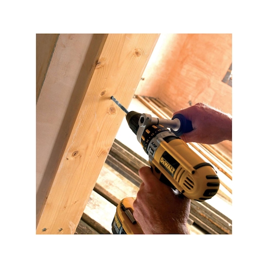 A person using a DEWALT cordless drill to drill a hole in a wooden beam in an indoor construction setting.