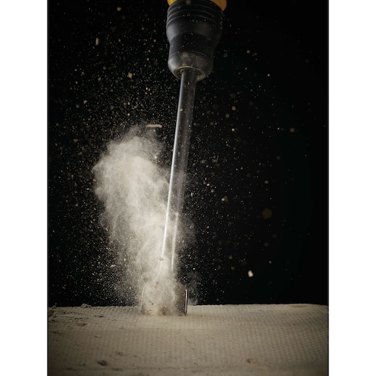 A DEWALT DT6824 chisel bit striking a concrete surface, creating a cloud of dust and debris, photographed against a dark