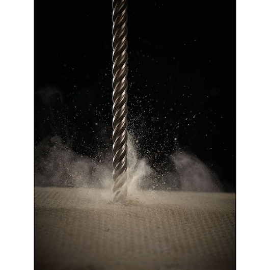 Close-up of a metal drill bit in action, drilling into a hard surface with dust particles flying in the air.