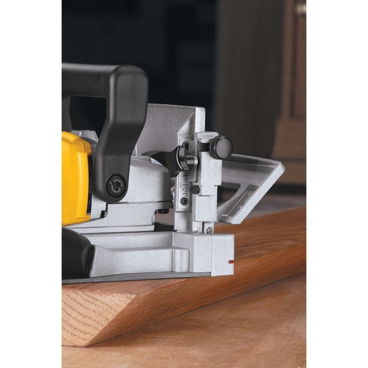 Close-up view of a DEWALT biscuit joiner DW682K being used on a wooden board. The tool's metal and plastic parts, adjustment knobs, and guide are clearly visible.