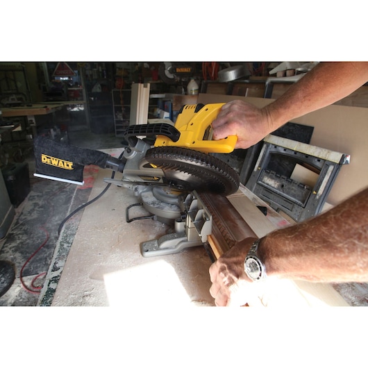 A person uses a DEWALT miter saw to cut a piece of wood in a workshop.