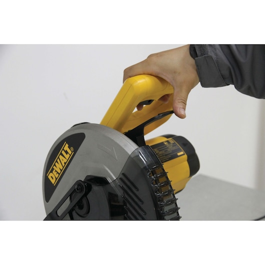 Close-up of a person’s hand holding the yellow handle of a DEWALT circular saw.
