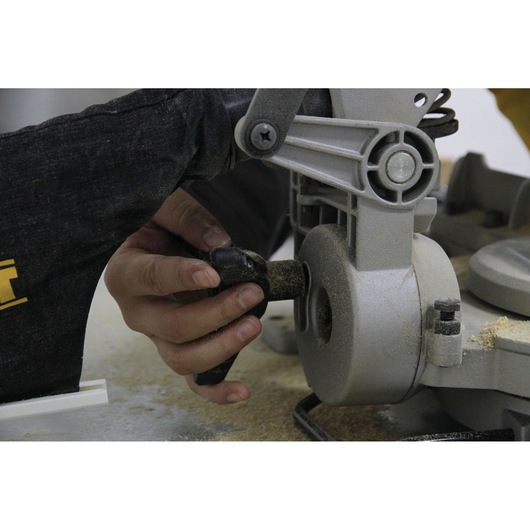 Close-up of a person adjusting a part on a DEWALT miter saw, with sawdust visible around the tool.