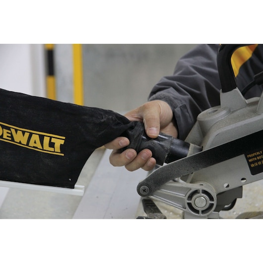Close-up of a person attaching a black DEWALT dust collection bag to a miter saw.