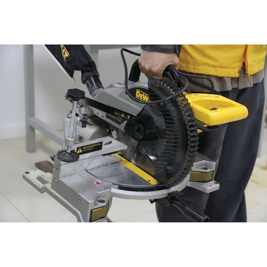 A person is holding a DEWALT DW714 miter saw, a professional power tool used for precise wood cutting in photography and carpentry applications.