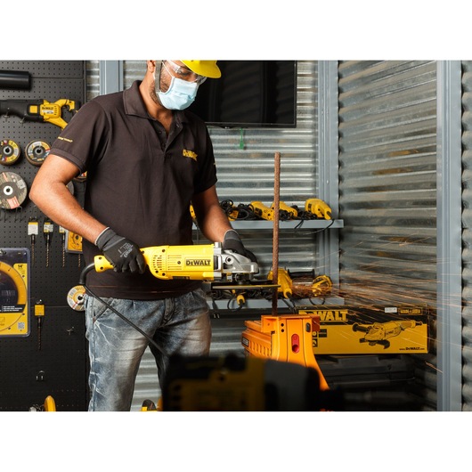 Person using a DEWALT DWE492 angle grinder to cut metal, with sparks in a workshop setting.