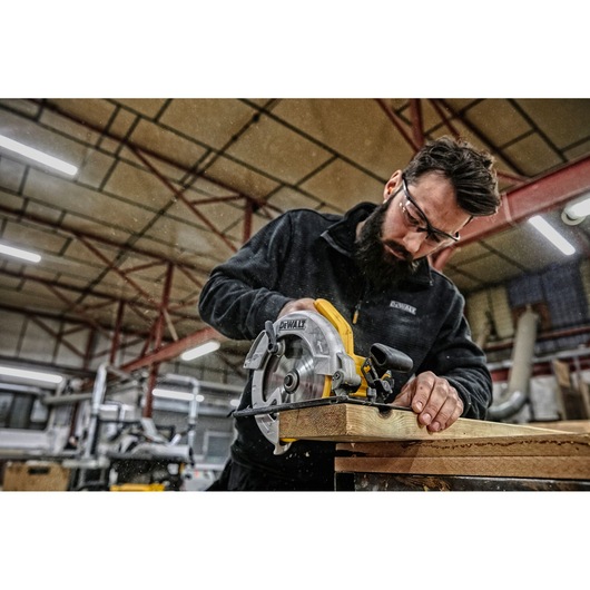 A person using a DEWALT circular saw (model DWE560) to cut a piece of wood in a workshop. The person's face is blurred for privacy.