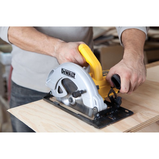 A person using a DEWALT DWE560 circular saw to cut a piece of wood. The tool features a yellow handle and a silver blade housing.