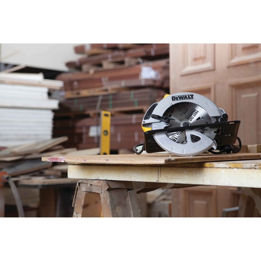 A DEWALT DWE560 circular saw placed on a wooden workbench in a workshop with stacks of wood in the background.