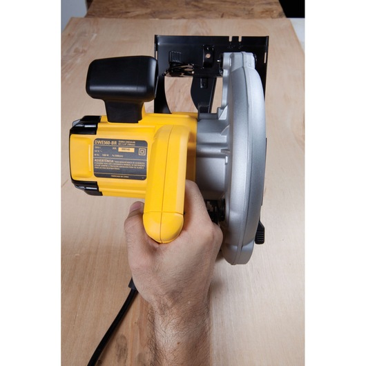 A close-up view of a person holding a DEWALT DWE560 circular saw, positioned on a wooden surface.