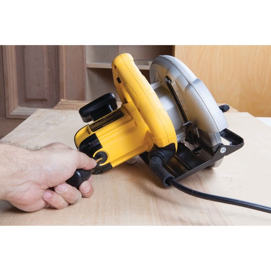 A person using a yellow and silver DEWALT DWE560 circular saw to cut wood, with the tool plugged in and held firmly.