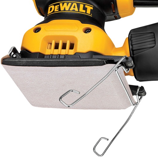 Close-up view of a DEWALT electric hand sander with a rectangular sanding pad attached, featuring metal clips to secure the sandpaper. The tool has a yellow and black design.