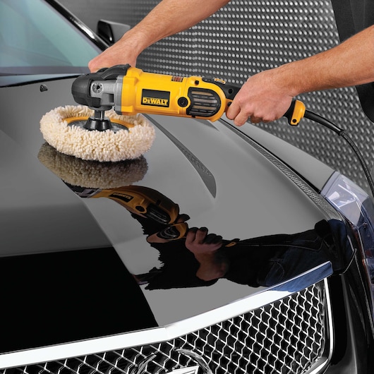 A person uses a DEWALT DWP849X electric polisher on the hood of a black car, polishing the surface with a wool pad.