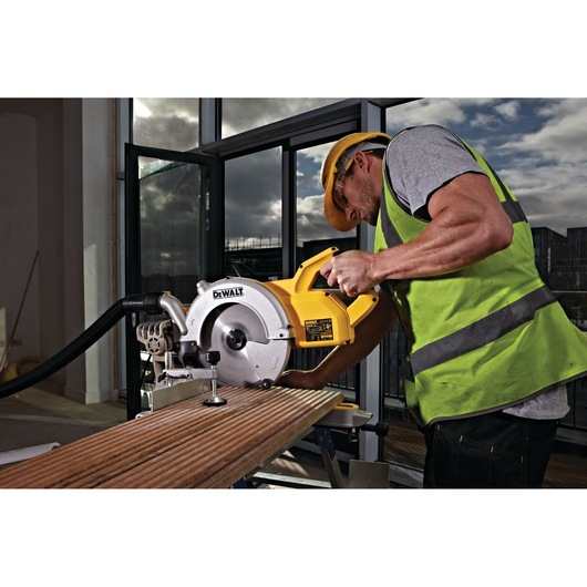Worker using a DEWALT DWS778 saw to cut wood indoors, wearing a safety vest and helmet.
