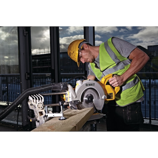 A person wearing a safety vest and hard hat is operating a DEWALT DWS778 miter saw to cut a wooden beam on a construction