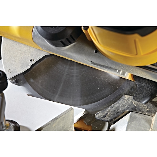 Close-up of a DEWALT DWS778 miter saw cutting wood, focusing on the blade and dust.