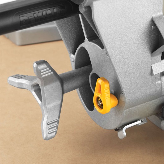 Close-up view of a DEWALT miter saw adjustment handle and locking knob, featuring silver and yellow parts, on a brown background.