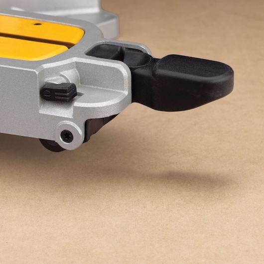 Close-up view of a DEWALT DWS780 miter saw component, showing a metallic silver part with yellow accents and a black plastic handle on a beige surface.