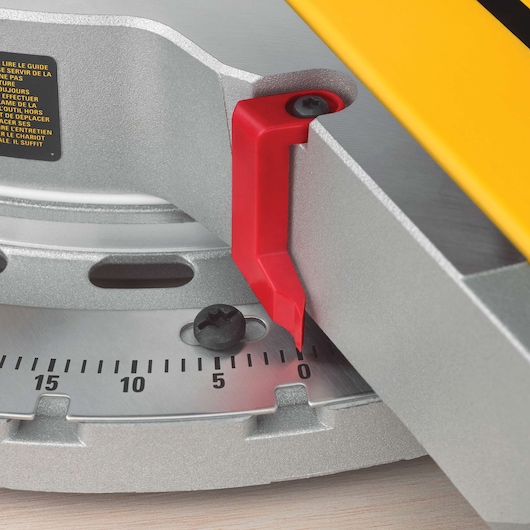 Close-up image of the angle adjustment scale on a DEWALT miter saw, showing a red indicator pointing to the zero degree mark on the metal scale.