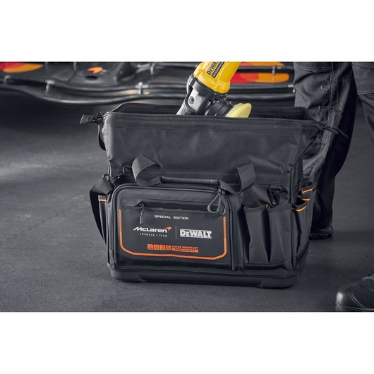 DEWALT McLaren tool bag with multiple compartments, black with orange accents, shown in a workshop setting.